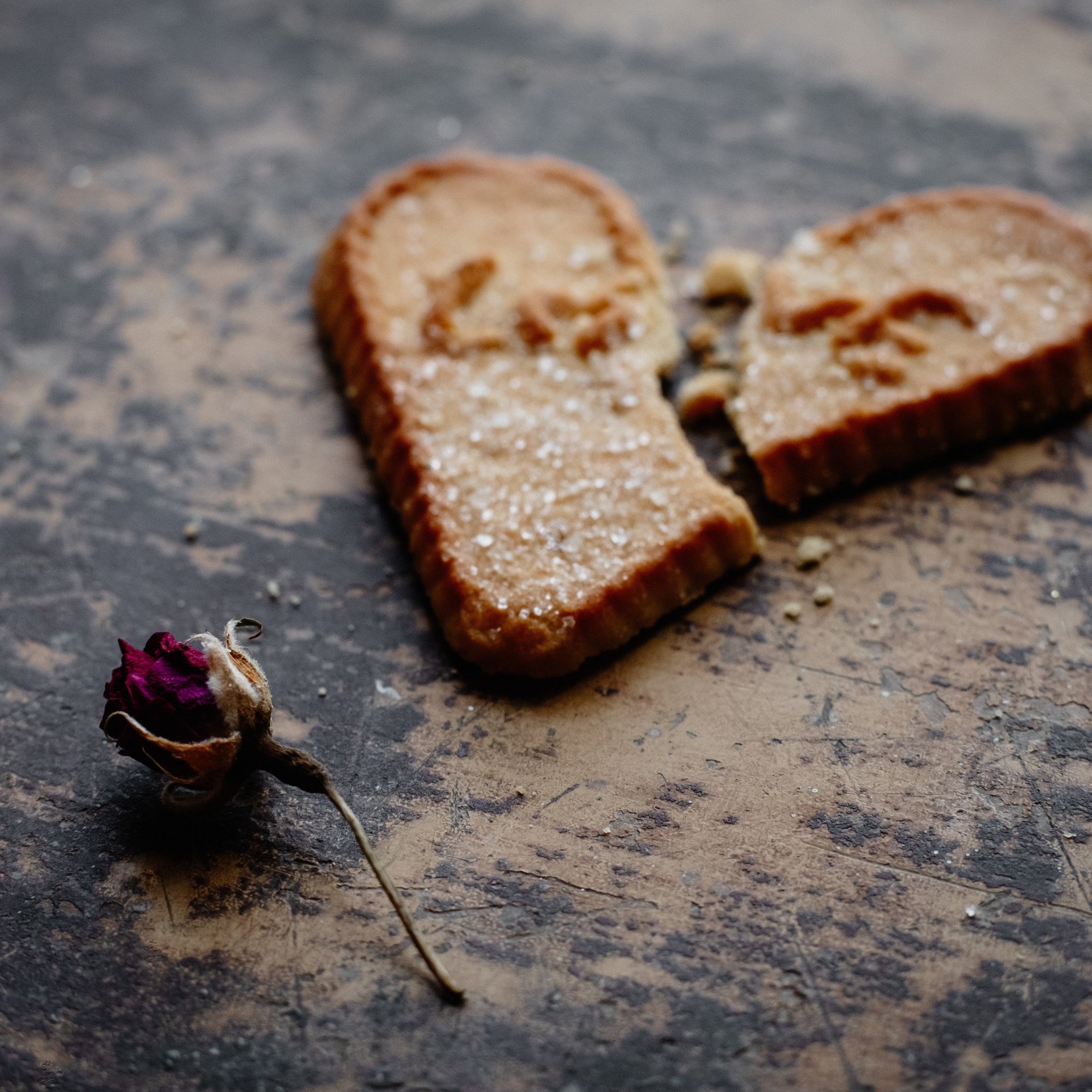 A dry rose and broken cookie that says love lying on a brown table