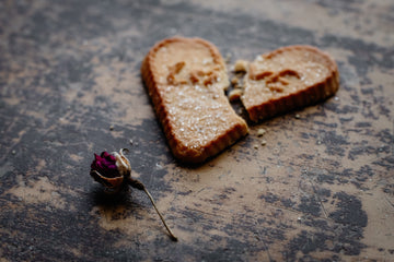 A dry rose and broken cookie that says love lying on a brown table