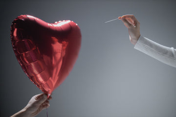 Person Holding Red Heart Balloon And Another Person Holding A Needle