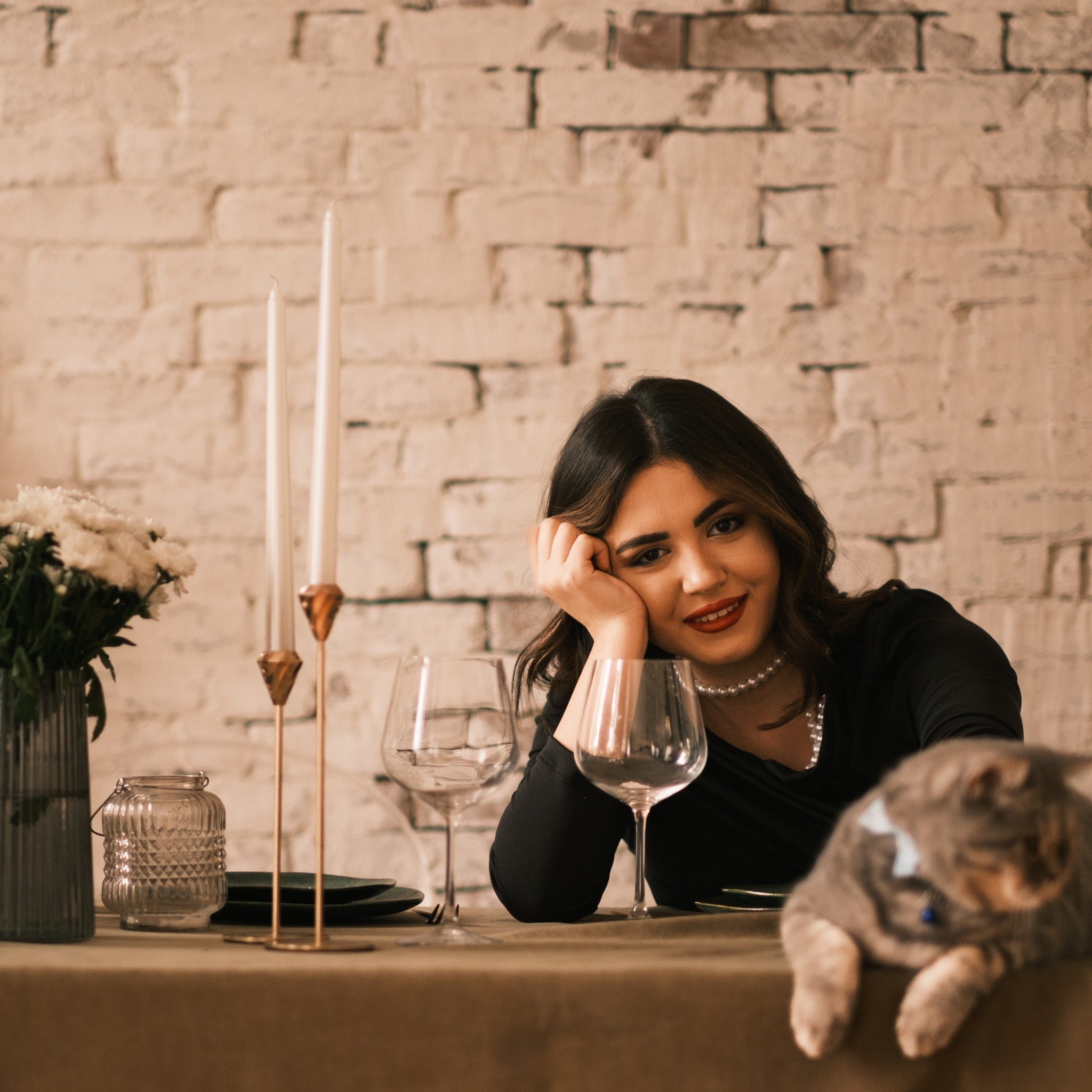 Woman in black long-sleeve dress smiling and petting a cat