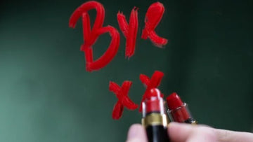 A person writing ‘bye’ on a mirror with a red lipstick