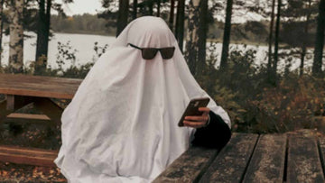 A person dressed up as a ghost, holding a phone