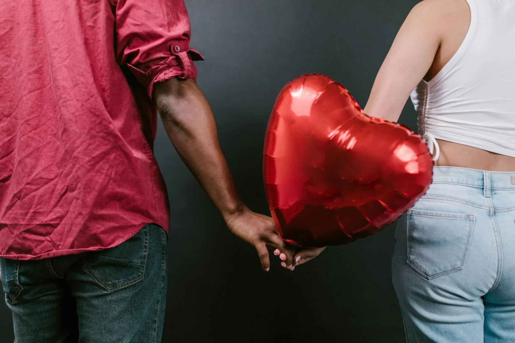 Two Persons Holding a Red Heart Shaped Balloon To Represent Best Valenine Gift For Boyfriend