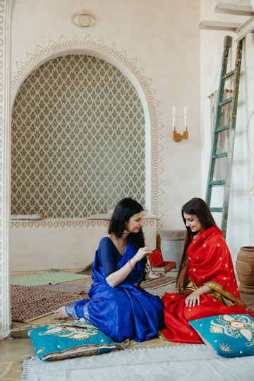 Two Indian women in bright saris sitting on the floor at home, mid conversation