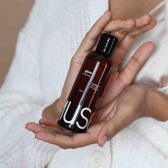A hand holding the 100ml Glow Relaxing bottle with another hand gently supporting and caressing it