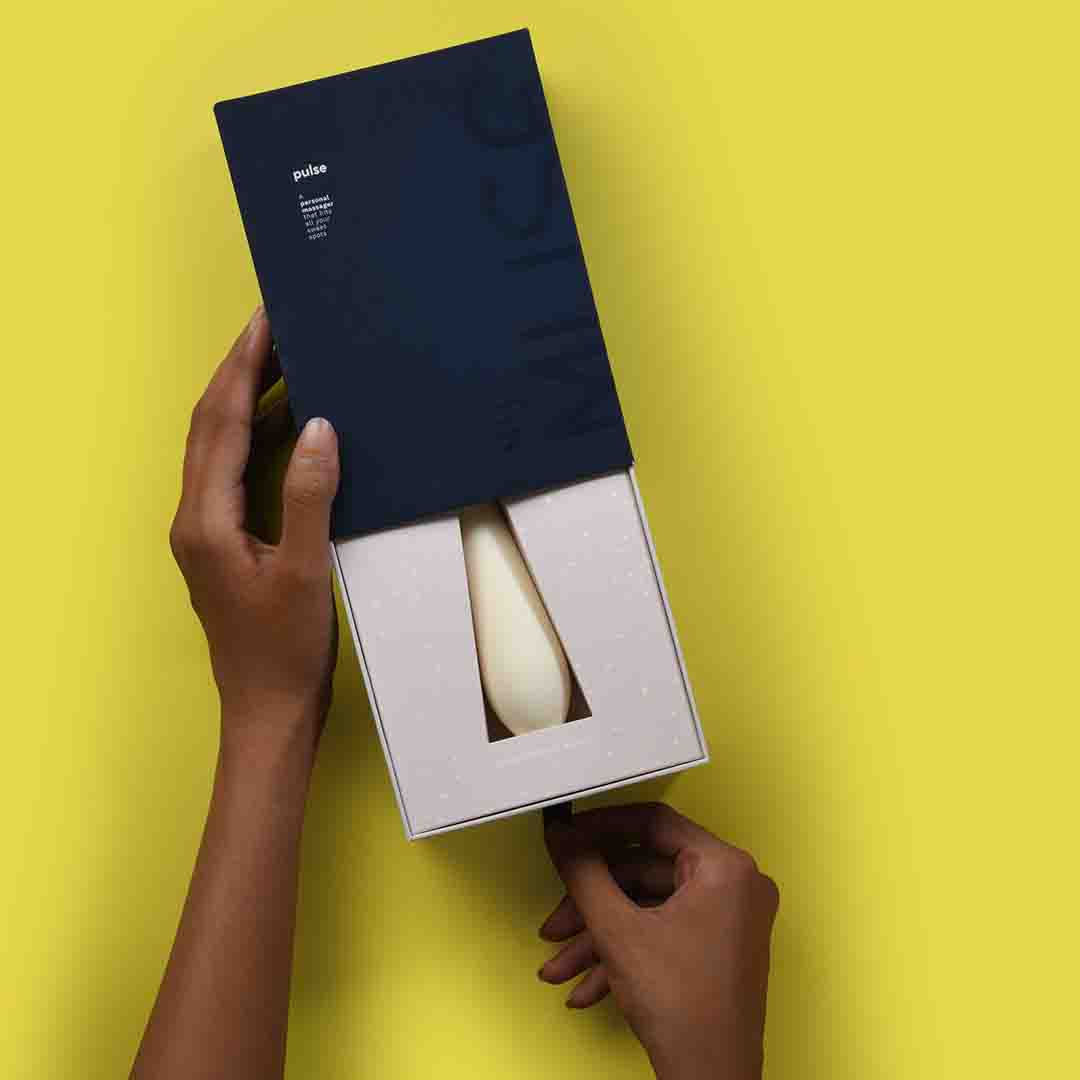 Top view of Pulse – a full body massager inside its packaging with the box being opened by a hand