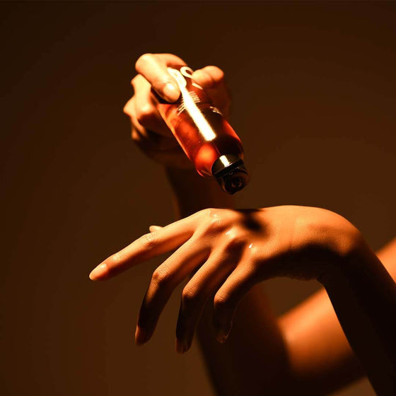 A person applying Glow Arousing massage oil on their hands for self-care in lit dark background