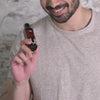 A man is holding a bottle of MyMuse's Glow Arousing Massage Oil, then pours the oil on a lady's shoulder and massages it